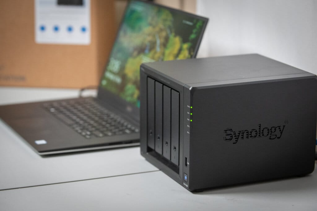 Synology NAS device next to a laptop with active LED indicators.