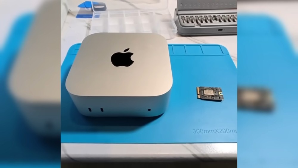 A close-up view of an Apple M4 Mac Mini next to a small circuit board, on a blue repair mat.