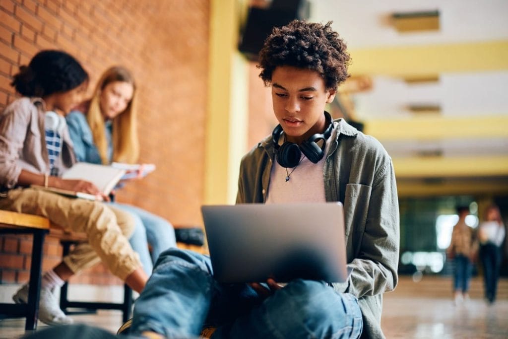 Best laptops for students. Young man with headphones, using a laptop in a school hallway