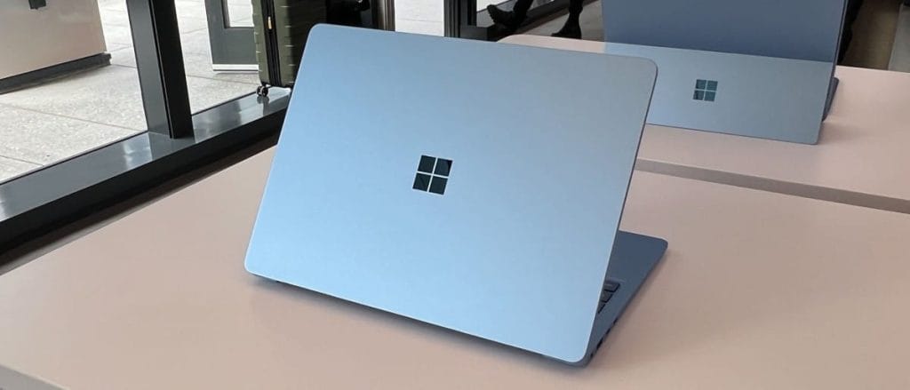 Blue Microsoft Surface Laptop 7 with a logo on the lid, placed on a desk in a modern office.