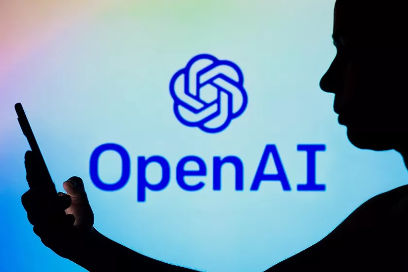 Image of a person's silhouette holding a smartphone against the backdrop of the OpenAI logo.