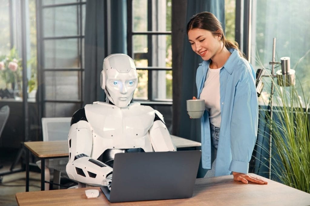 A woman and a humanoid robot interacting in a modern office, working on a laptop