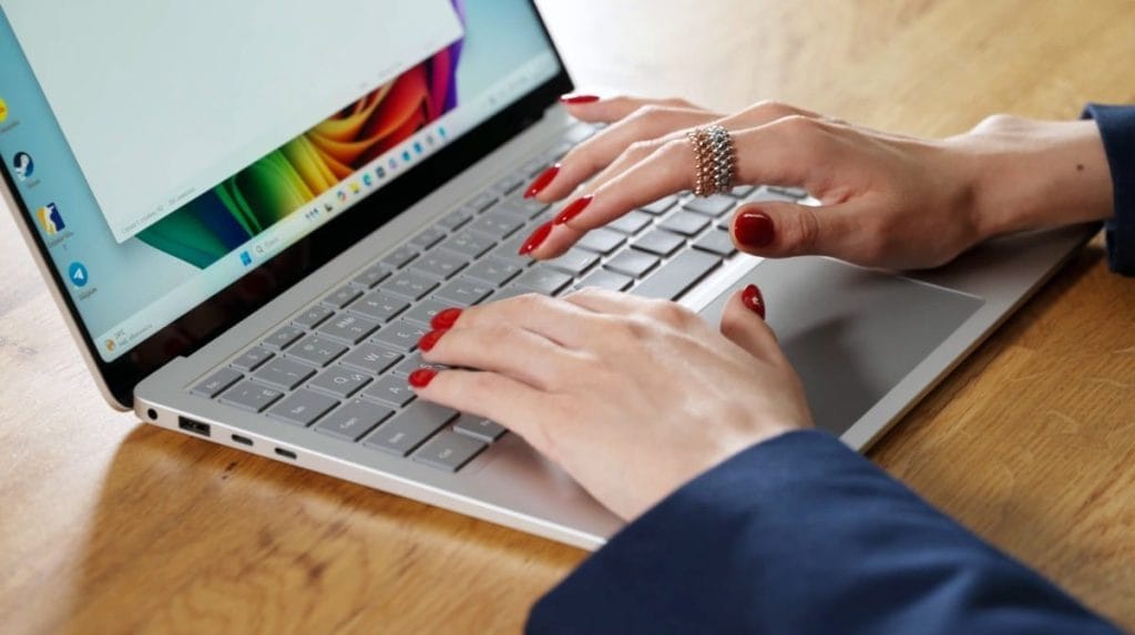 Woman typing on a silver Surface Laptop 7 on a wooden table