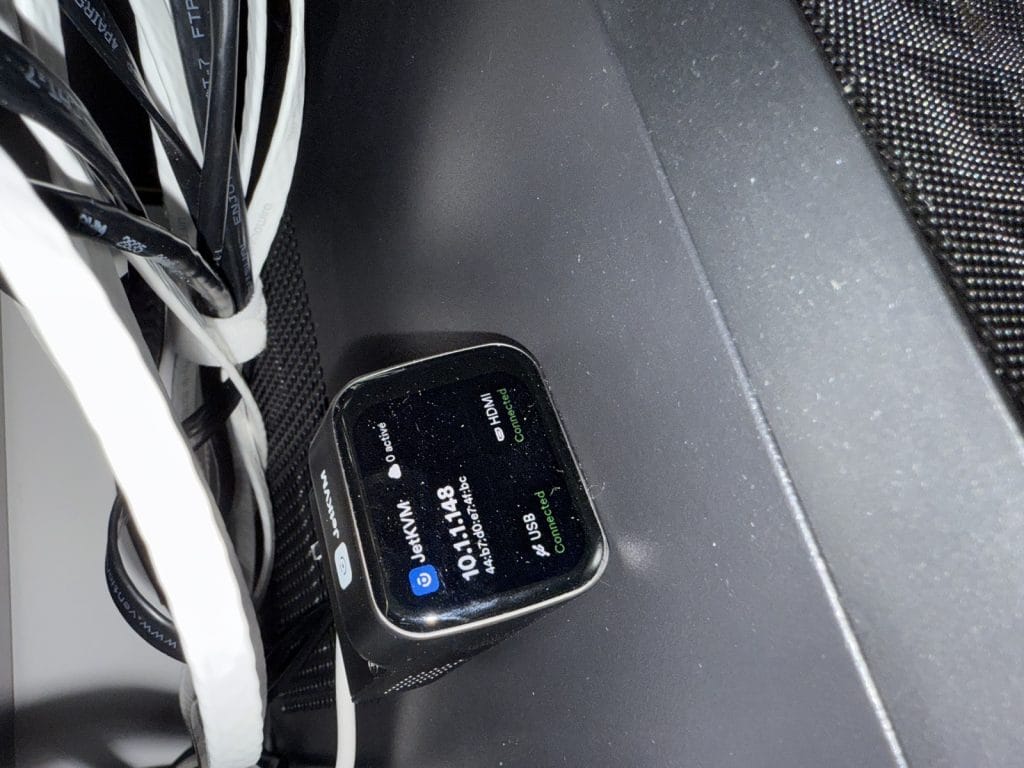 A close-up view of a JetKVM device displaying connection statuses under tangled cables