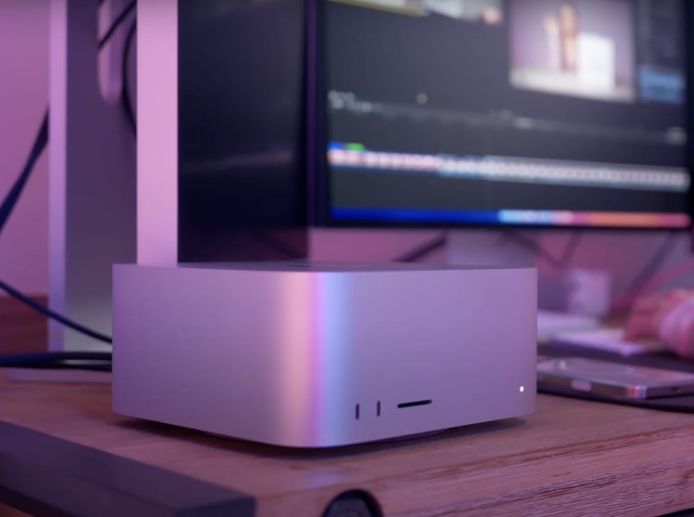 A sleek silver computing device next to a computer monitor displaying an editing software interface.