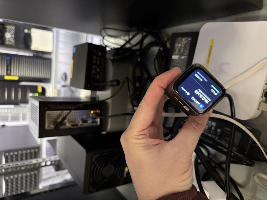 A hand holding a JetKVM displaying network information amidst server equipment