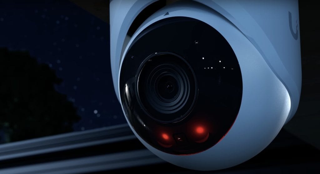 A close-up of a night surveillance camera with red LED lights highlighting its lens.