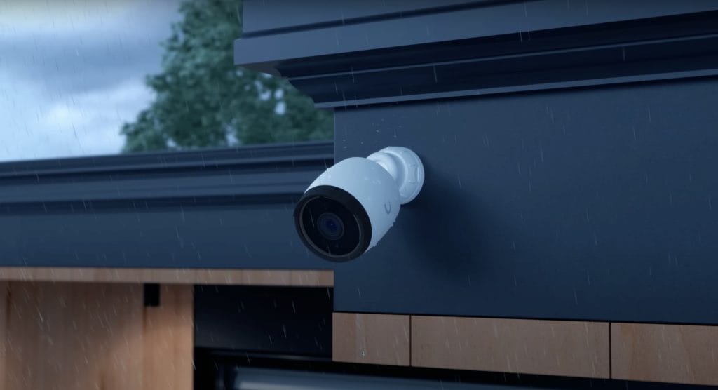 An outdoor security camera mounted on the wall of a modern home during a rainy day, showcasing weatherproof technology.
