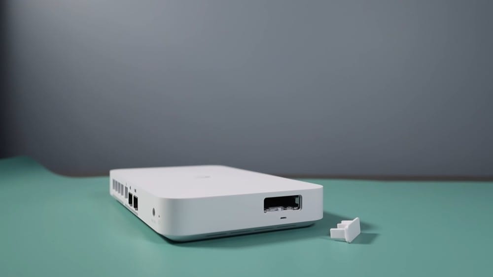A sleek white device with ports, ideal for networking, sits on a teal surface, accompanied by a small plastic connector piece.