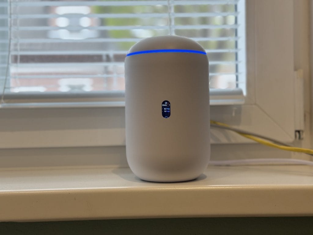 UniFi Dream Router 7. Modern white smart Wi-Fi router with LED indicator and digital display on a windowsill