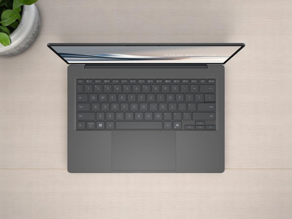 Asus Zenbook A14. Top view of a sleek Asus Zenbook laptop with a dark keyboard on a wooden desk next to a green potted plant