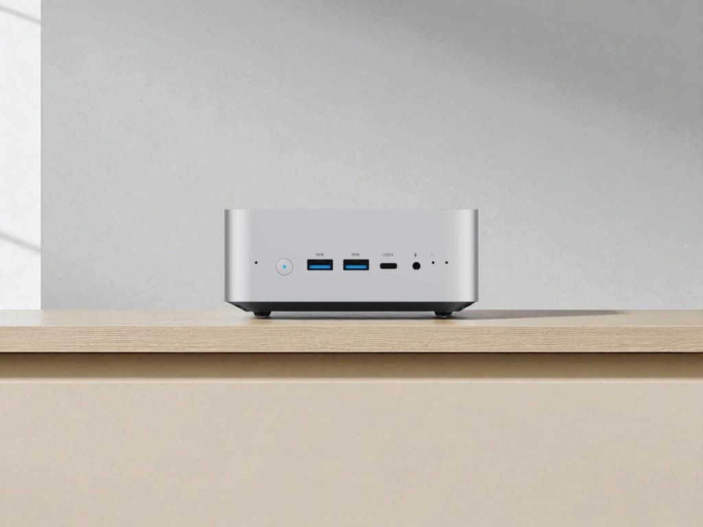 Minisforum AI X1 Review. A compact silver mini PC on a wooden surface with USB ports and 3.5mm audio jack on the front panel