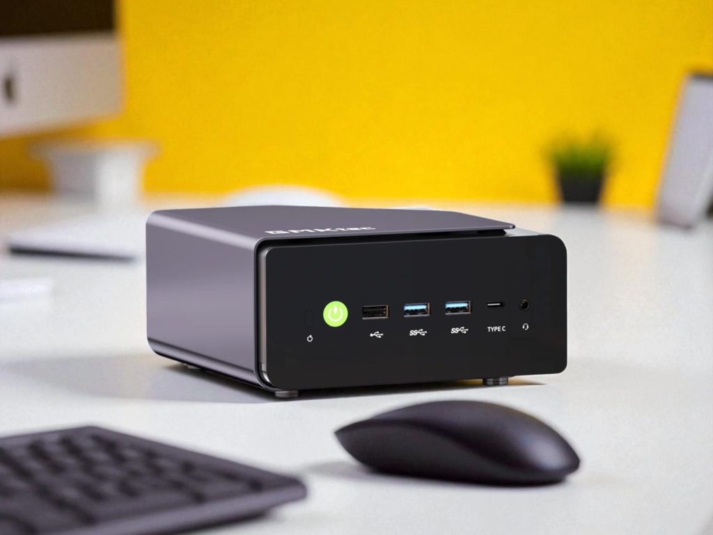 GMKtec K12 MiniPC Review: Big Upgrades, But Not for Everyone. A compact black mini PC on a white desk with USB ports, headphone jack, and a power button, alongside a wireless mouse and keyboard against a yellow background